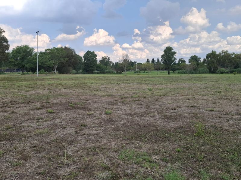 A wide, open residential plot featuring established trees and natural grass cover, offering a spacious setting for future development.