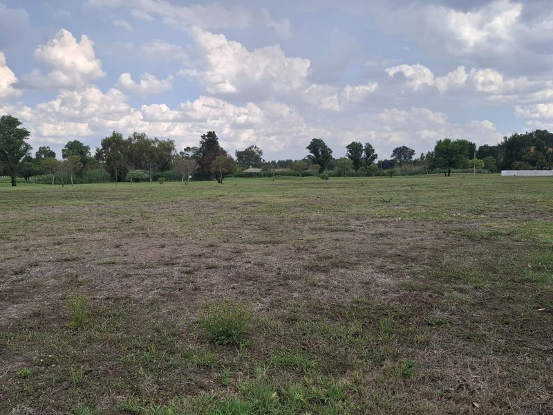 A wide-angle view of a vacant residential plot featuring open grassland under a cloudy sky.
