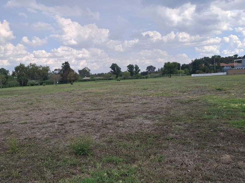 A wide, open vacant residential plot featuring level grass terrain and surrounding mature trees, offering a blank canvas for future development.