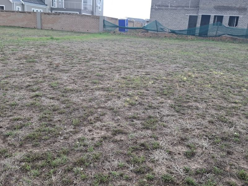 A vacant residential plot featuring a perimeter brick wall and temporary construction fencing, ready for development.