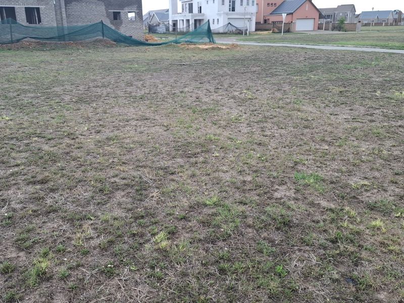 A view of a vacant residential plot of land in a developed estate, featuring cleared ground and surrounding residential construction.