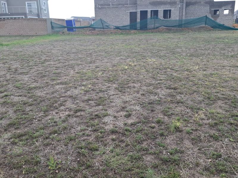 A vacant residential plot featuring sparse grass coverage, enclosed by a perimeter brick wall with construction fencing visible in the background.