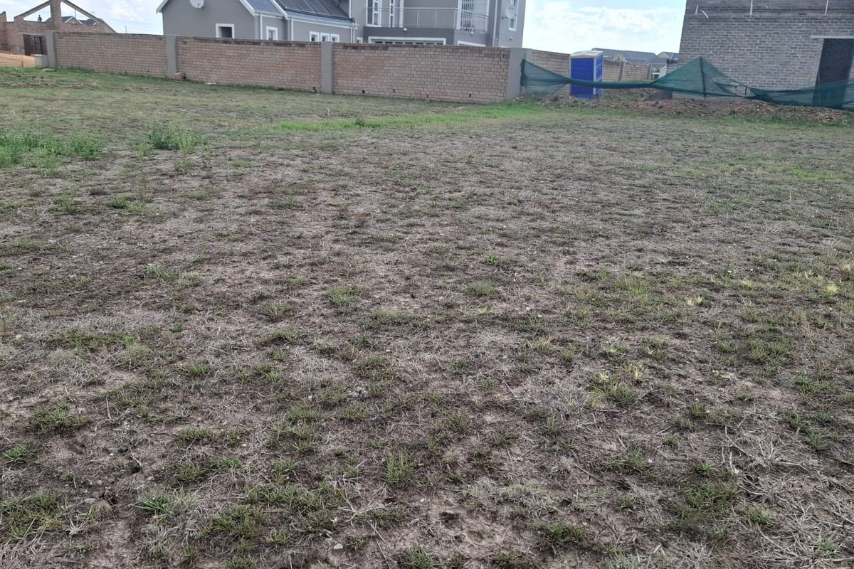 A vacant residential plot featuring a level grassed area enclosed by a perimeter boundary wall in a developing estate.