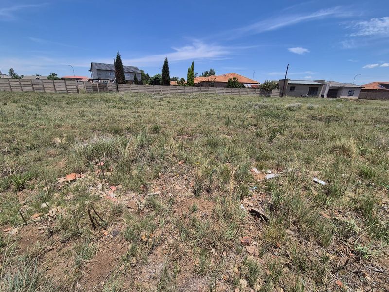 A vacant residential plot featuring natural grass cover and a precast concrete boundary wall, offering a clear space for future development.