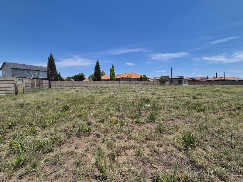 A vacant residential plot featuring natural grass coverage and enclosed by a precast concrete boundary wall.