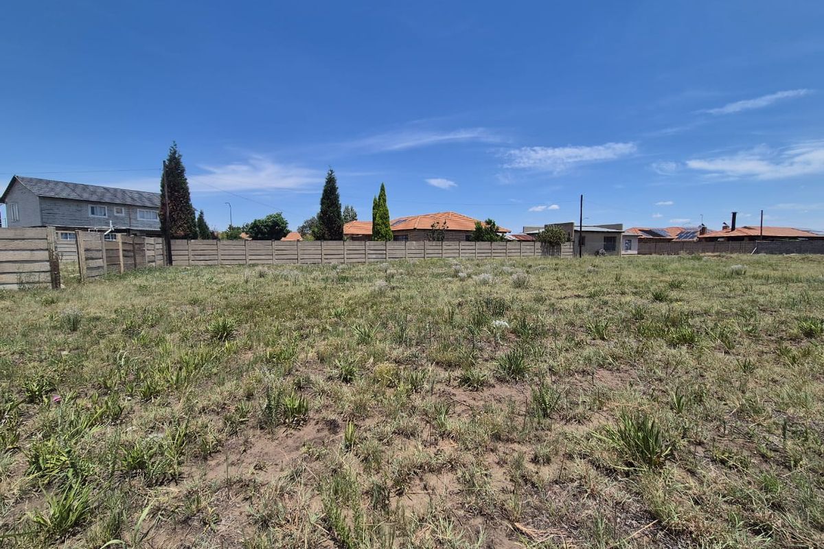 A vacant residential plot featuring natural grass coverage and enclosed by a precast concrete boundary wall.