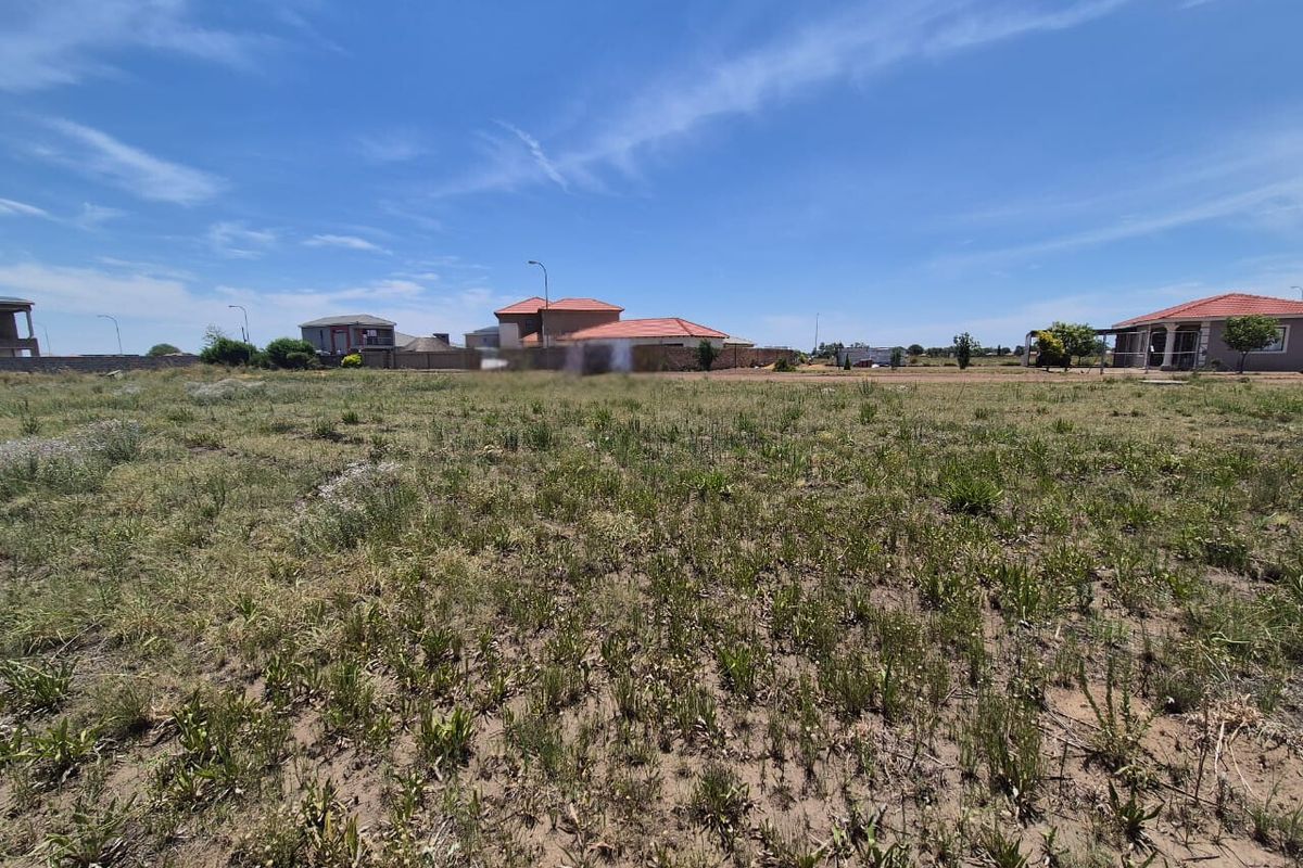 A vacant residential plot of land featuring natural grass cover and surrounding perimeter walling in a developed neighborhood.