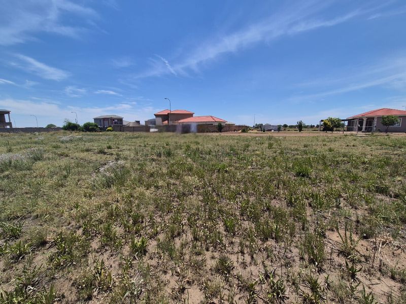 A vacant residential plot of land featuring natural grass cover and surrounding perimeter walling in a developed neighborhood.