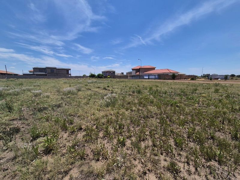 A view of a vacant residential plot of land with surrounding boundary walls and neighboring houses in the distance.