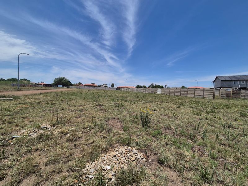 A vacant residential plot featuring natural grass cover, enclosed by a precast concrete boundary wall, situated in a developed neighborhood.