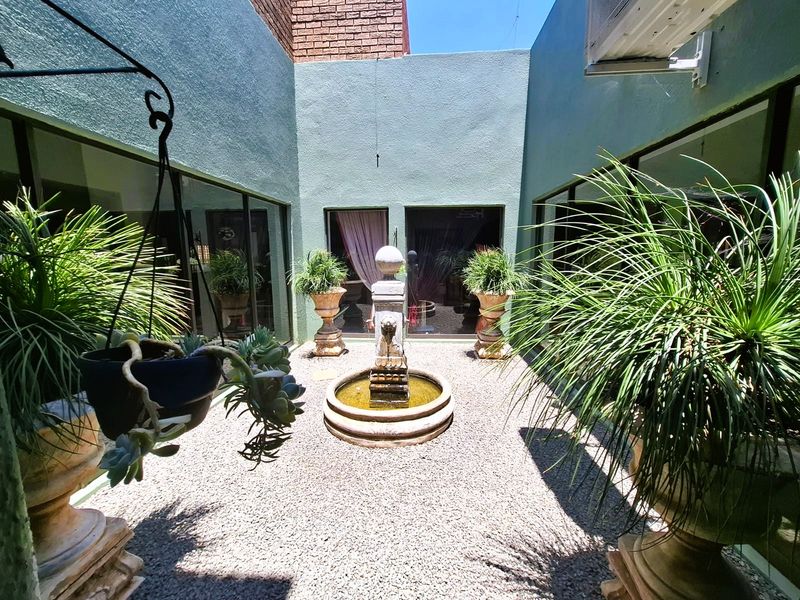 A private, enclosed courtyard featuring a central stone fountain, gravel flooring, and large glass sliding doors providing access to the interior living spaces.