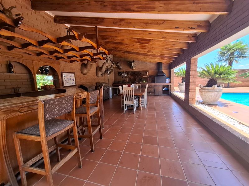 Spacious covered patio featuring a built-in bar, exposed timber beams, and a built-in braai, overlooking the swimming pool area.