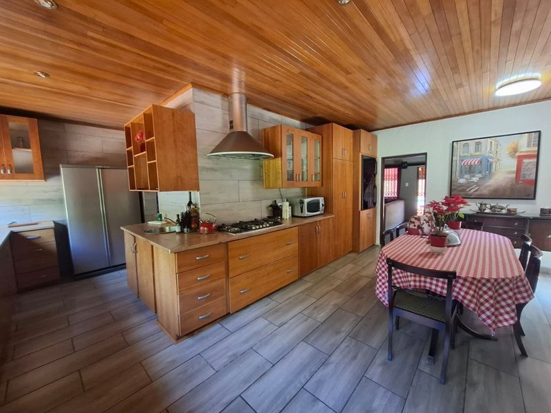 Open-plan kitchen and dining area featuring warm wooden cabinetry, a gas hob with extractor, and a distinctive timber-clad ceiling.