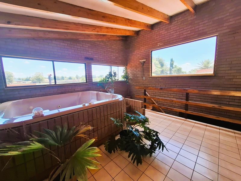 Spacious bathroom featuring a built-in spa bath, exposed timber ceiling beams, face brick walls, and large windows providing ample natural light.
