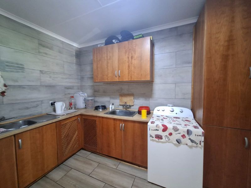 A functional laundry room featuring built-in wooden cabinetry, a stainless steel sink, and tiled wall finishes.