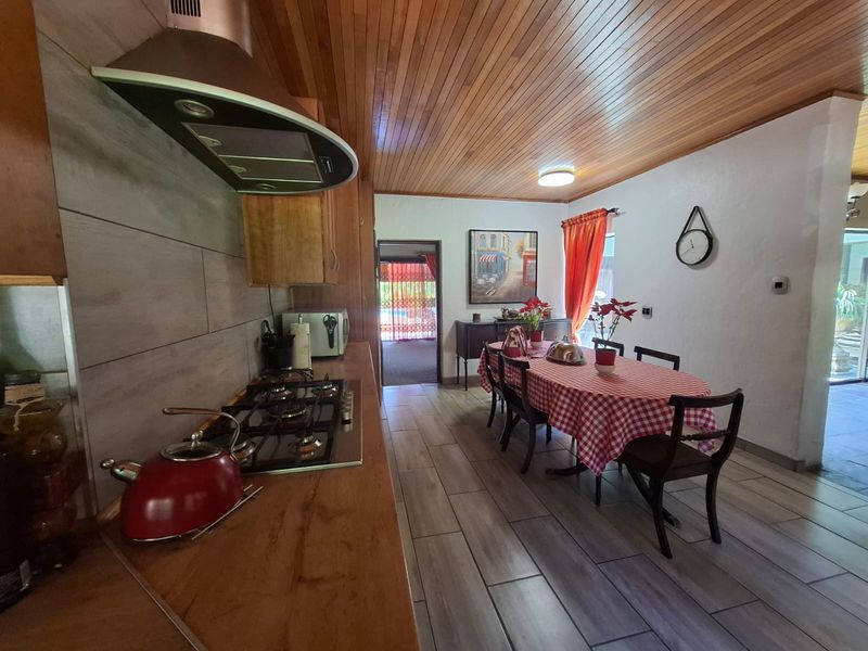 Open-plan kitchen and dining area featuring a gas hob, extractor fan, warm wooden ceiling, and modern tiled flooring.
