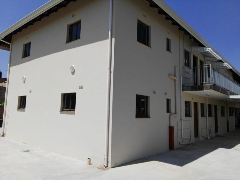 Rear exterior view of the townhouse complex featuring a concrete driveway, multi-level facade, and a balcony with metal railings.