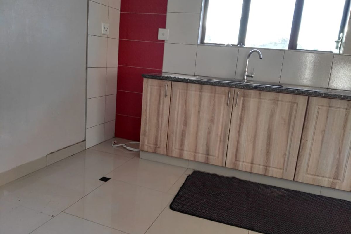 A functional kitchen area featuring light wood-finish cabinetry, granite countertops, a stainless steel sink, and a tiled splashback with a red accent feature.