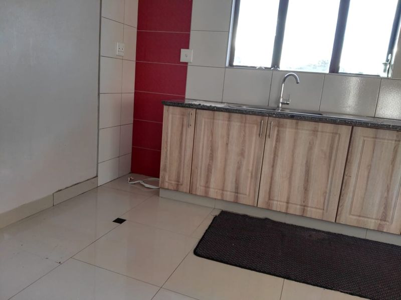 A functional kitchen area featuring light wood-finish cabinetry, granite countertops, a stainless steel sink, and a tiled splashback with a red accent feature.