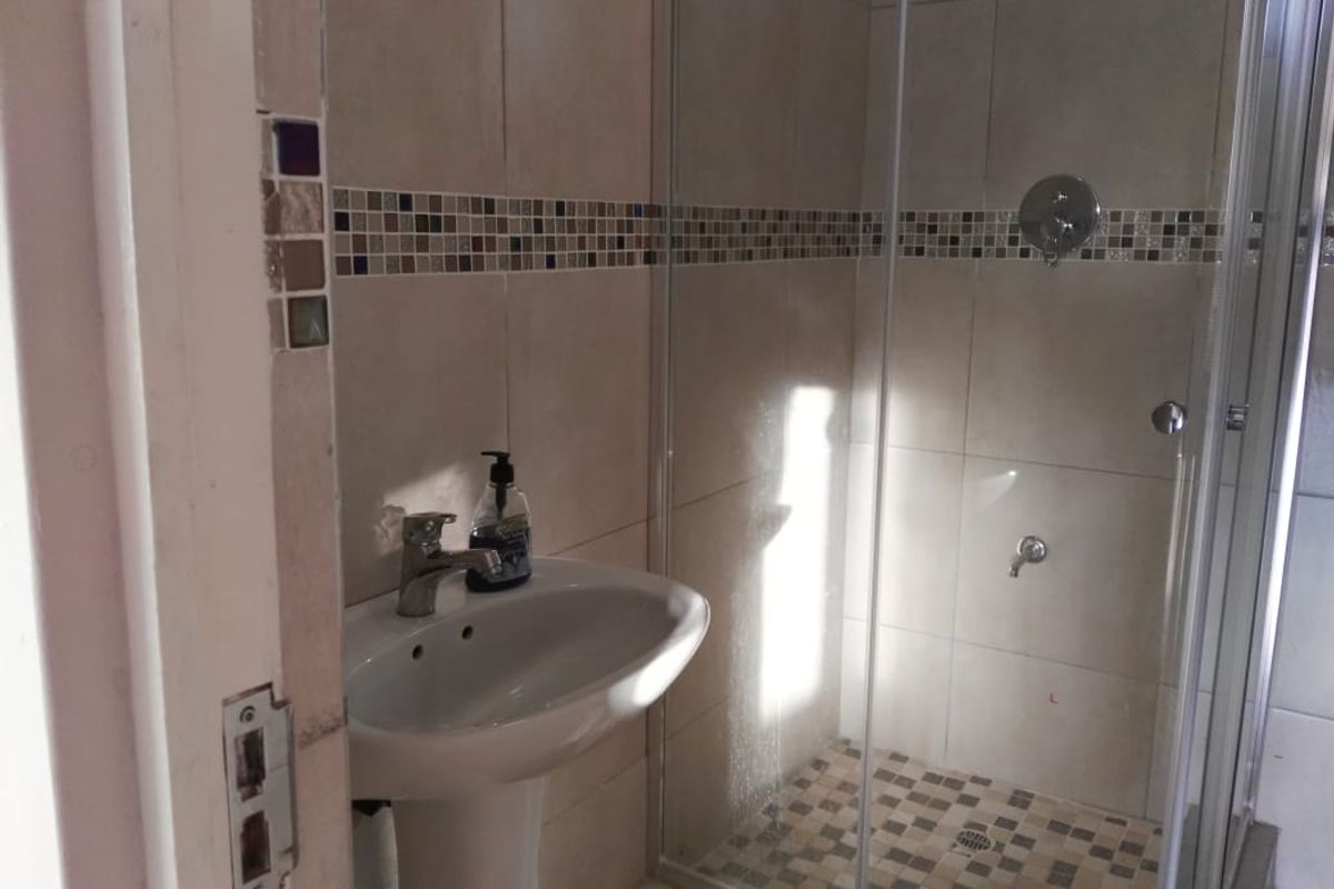 A functional bathroom featuring a pedestal basin, a glass-enclosed shower, and decorative mosaic tile accents.