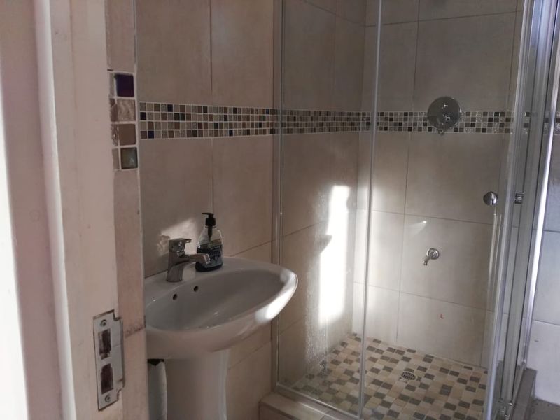 A functional bathroom featuring a pedestal basin, a glass-enclosed shower, and decorative mosaic tile accents.