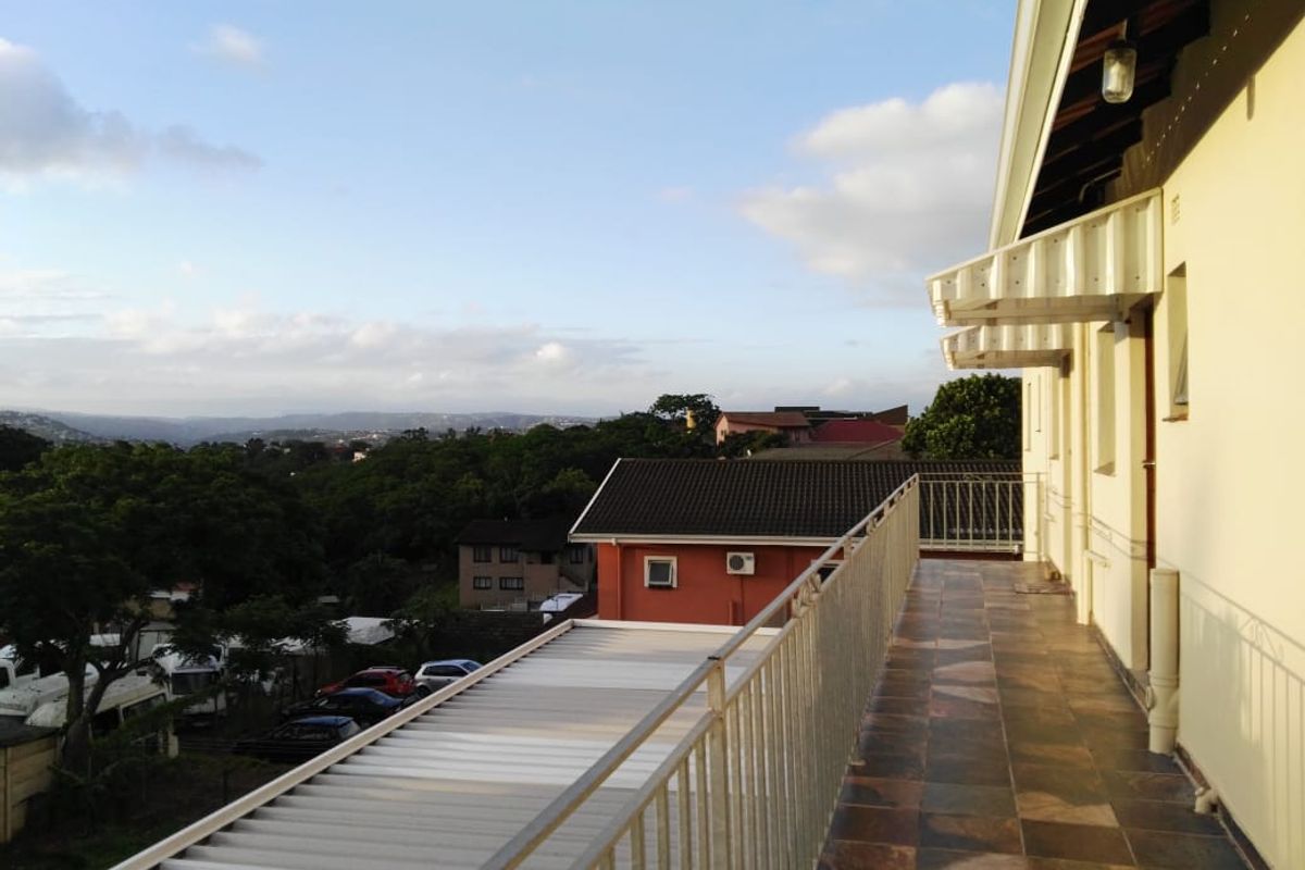 A spacious elevated balcony featuring tiled flooring, a protective metal balustrade, and an awning, offering expansive views of the surrounding neighborhood.