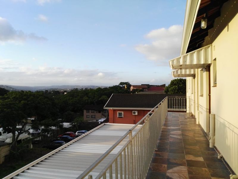 A spacious elevated balcony featuring tiled flooring, a protective metal balustrade, and an awning, offering expansive views of the surrounding neighborhood.