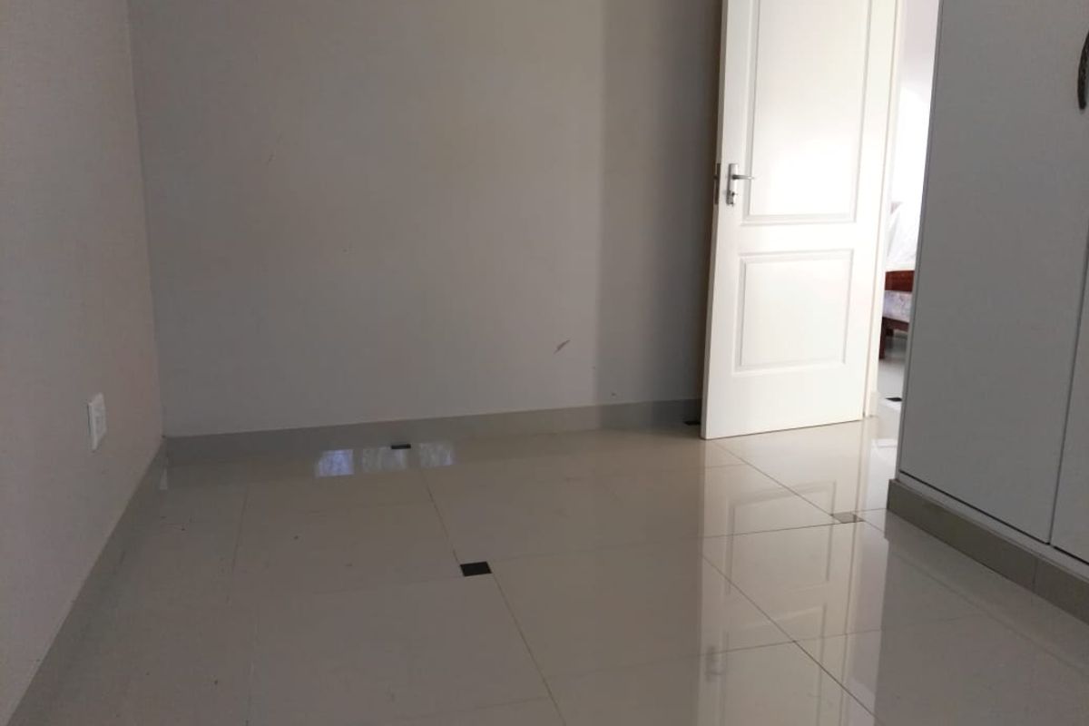 An empty bedroom featuring neutral tiled flooring and a built-in wardrobe, offering a clean and versatile space ready for personalization.