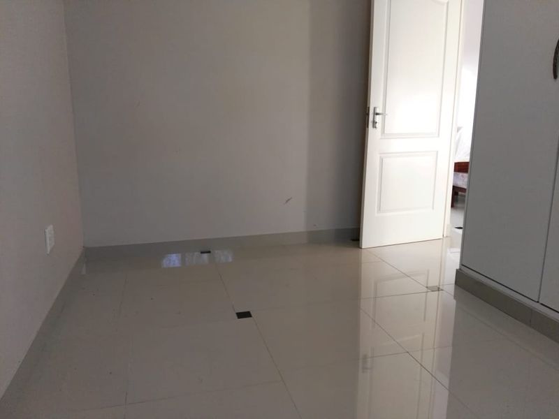 An empty bedroom featuring neutral tiled flooring and a built-in wardrobe, offering a clean and versatile space ready for personalization.