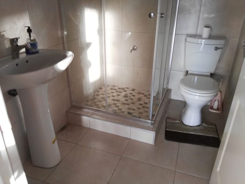 A functional bathroom featuring a pedestal basin, a glass-enclosed shower with tiled flooring, and a standard toilet.