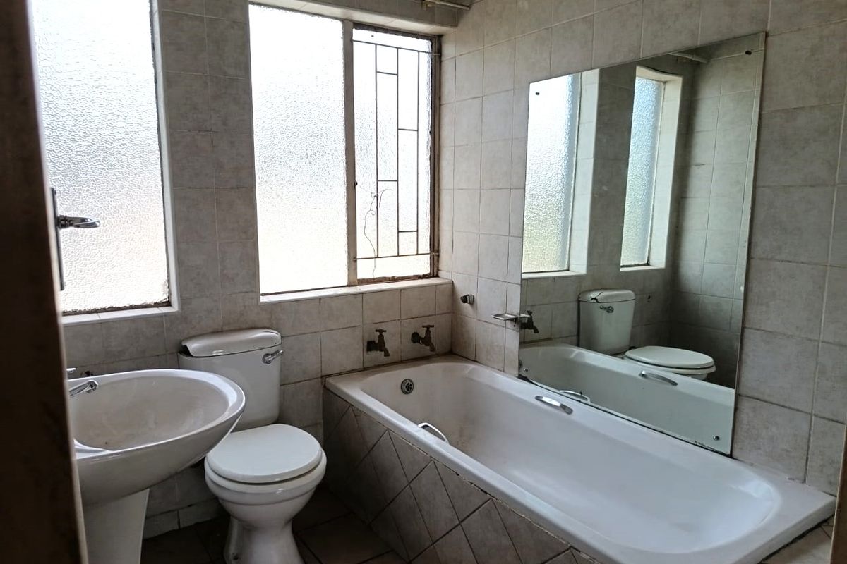A dated bathroom featuring a pedestal basin, toilet, and bathtub with tiled finishes, requiring cosmetic updates to modernize the space.