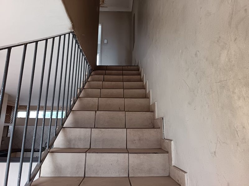 A staircase with tiled steps and a metal balustrade, showing signs of wear and water damage on the ceiling.
