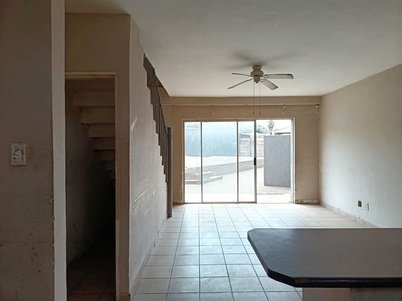 An open-plan living area featuring tiled flooring, a ceiling fan, and a staircase, with sliding glass doors providing access to the rear exterior.