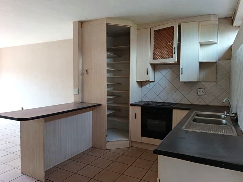 A dated kitchen featuring built-in cabinetry, a breakfast bar, integrated oven and hob, and tiled flooring, offering potential for modernization.