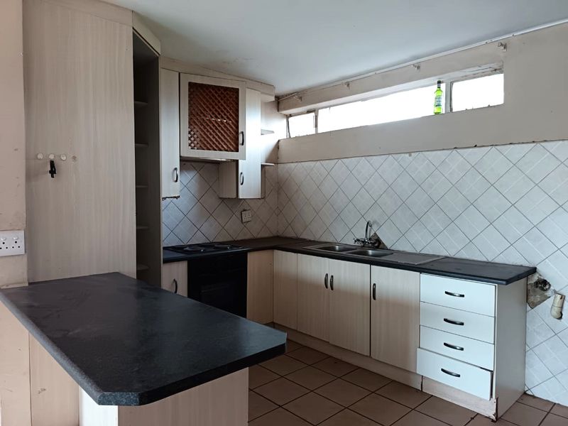A dated kitchen featuring built-in cabinetry, laminate countertops, a double sink, and an integrated oven, requiring cosmetic updates to modernize the space.