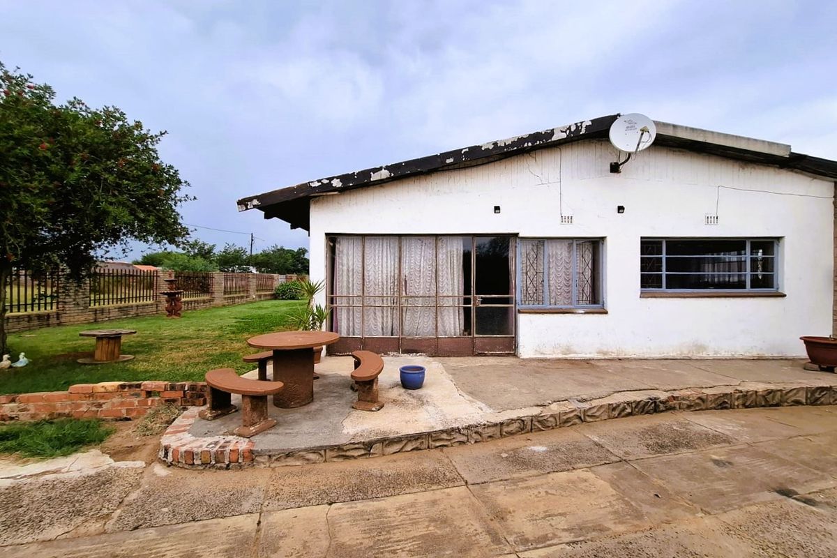 Rear exterior view of the house featuring a concrete patio area, metal security fixtures, and a spacious garden with brick boundary walling.