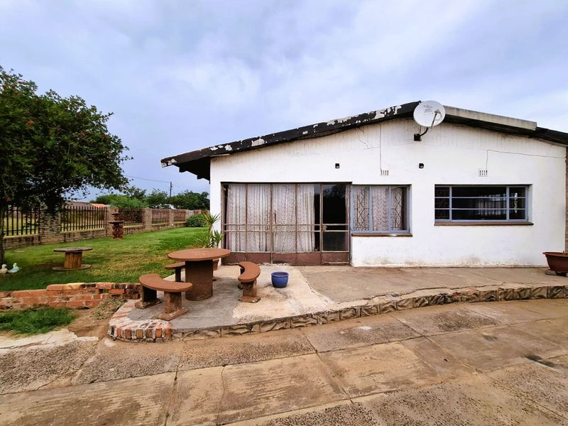 Rear exterior view of the house featuring a concrete patio area, metal security fixtures, and a spacious garden with brick boundary walling.