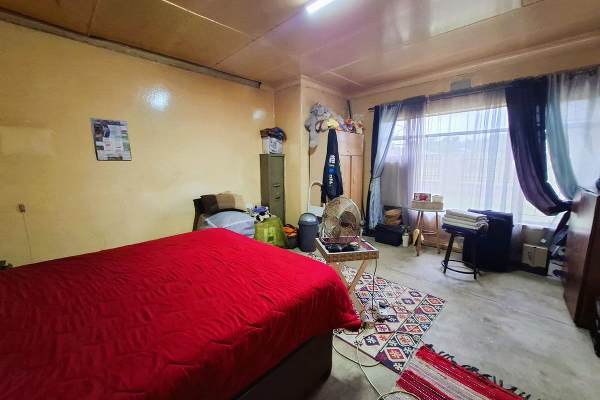 A bedroom featuring a large window, fluorescent lighting, and concrete flooring, currently requiring cosmetic updates to the walls and ceiling finishes.