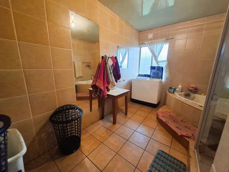 A functional bathroom featuring tiled walls and flooring, a built-in bathtub, and a shower enclosure, offering a practical layout for daily use.