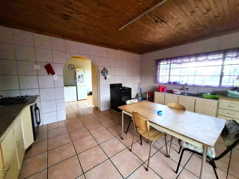 Spacious kitchen featuring tiled flooring, timber ceiling, and an archway leading to an adjacent utility area, offering potential for modernization.