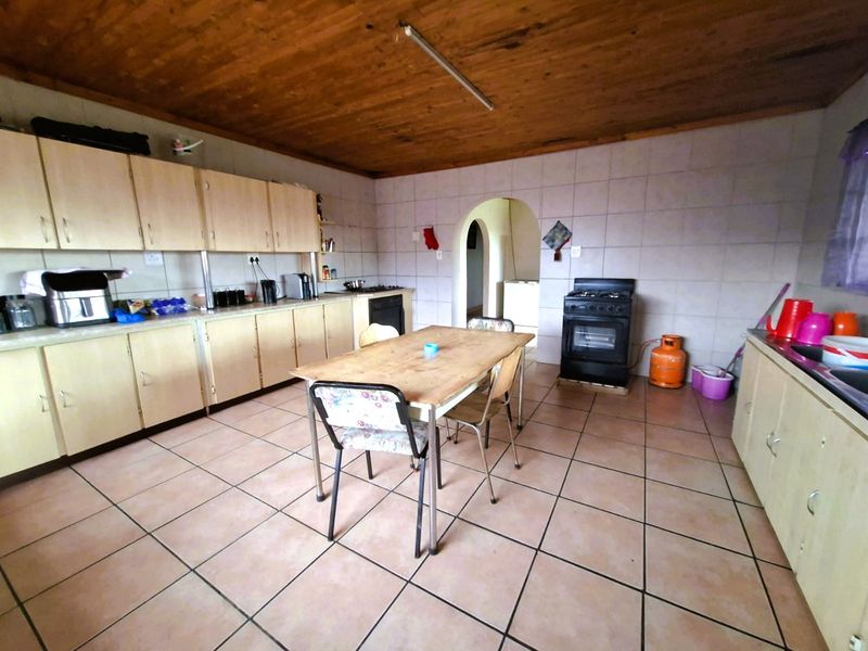 Spacious kitchen featuring timber ceilings, tiled flooring, extensive cabinetry, and a freestanding oven, offering a functional layout with potential for modern updates.