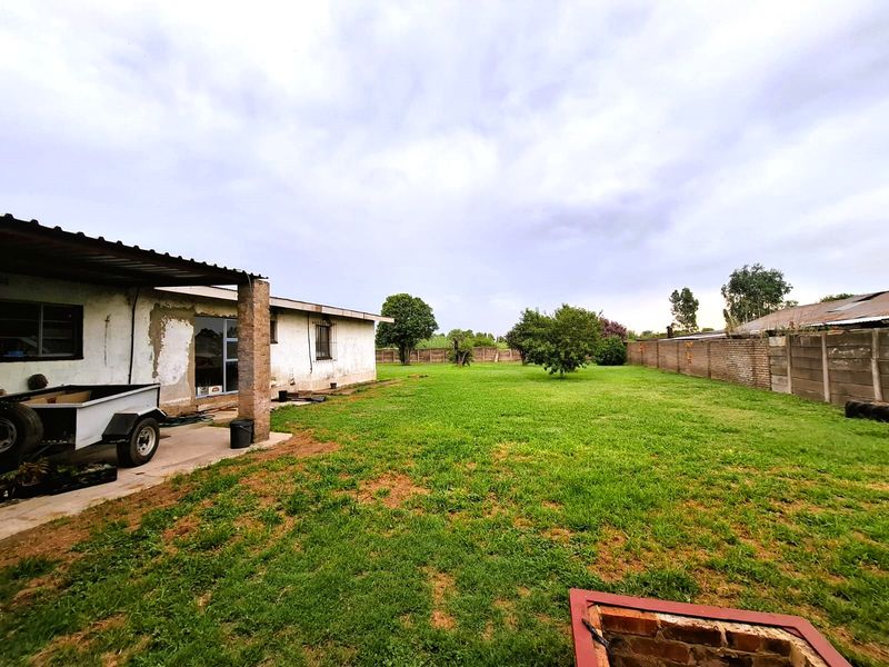 Spacious rear garden featuring a covered patio area, expansive lawn, and perimeter brick boundary walls, offering significant potential for landscaping and outdoor improvement.