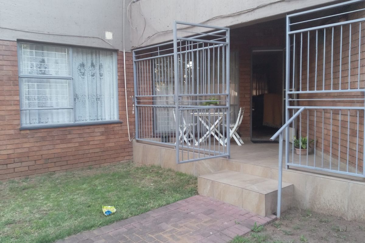Ground floor flat exterior featuring a tiled patio area, security gates, brick facade, and a small private garden space with a paved walkway.