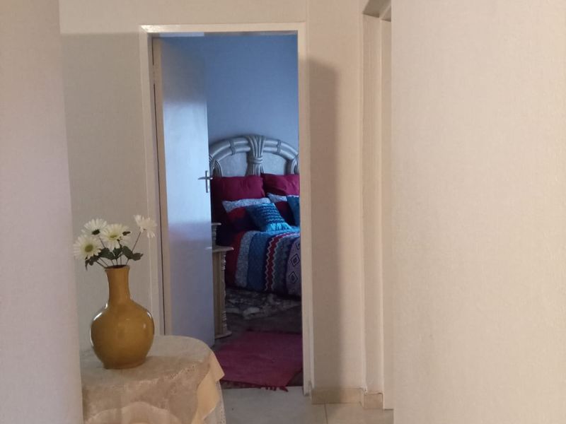 A view through a hallway leading into a bedroom, featuring neutral tiled flooring and plain white walls.