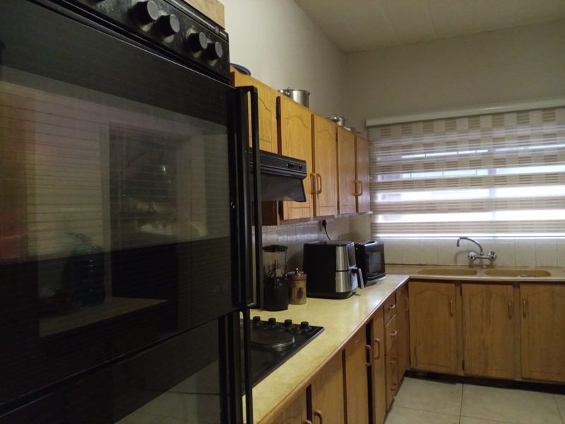 A functional kitchen featuring wooden cabinetry, a built-in oven, hob, extractor fan, and a double sink with roller blinds.