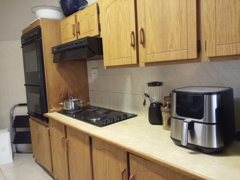A dated kitchen featuring wood-look laminate cabinetry, a built-in double oven, electric hob, and tiled backsplash, offering potential for a modern renovation.