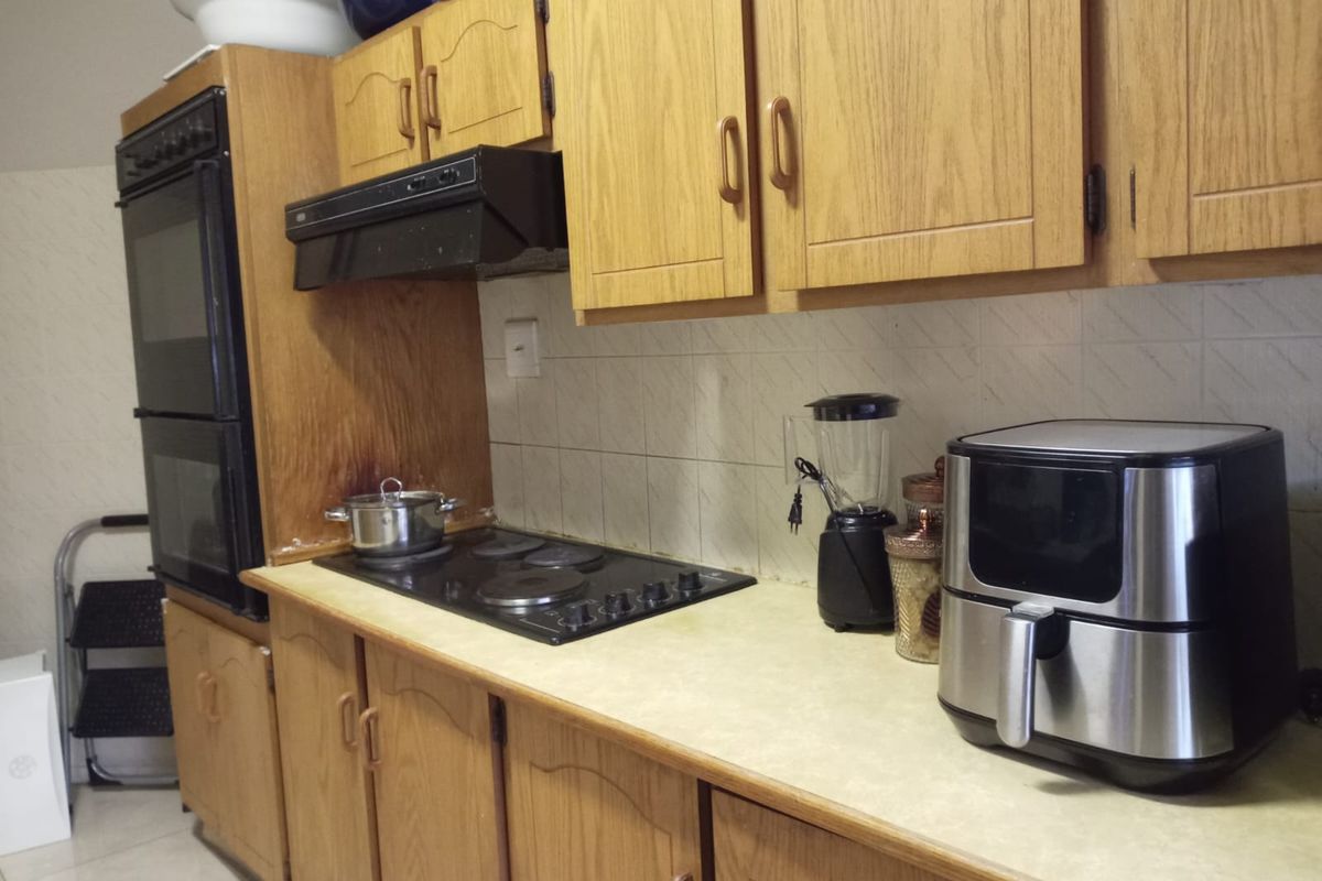 A dated kitchen featuring wood-look laminate cabinetry, a built-in double oven, electric hob, and tiled backsplash, offering potential for a modern renovation.