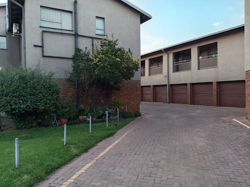 Exterior view of a residential flat complex featuring a paved driveway, multiple roller garage doors, and upper-level balconies.