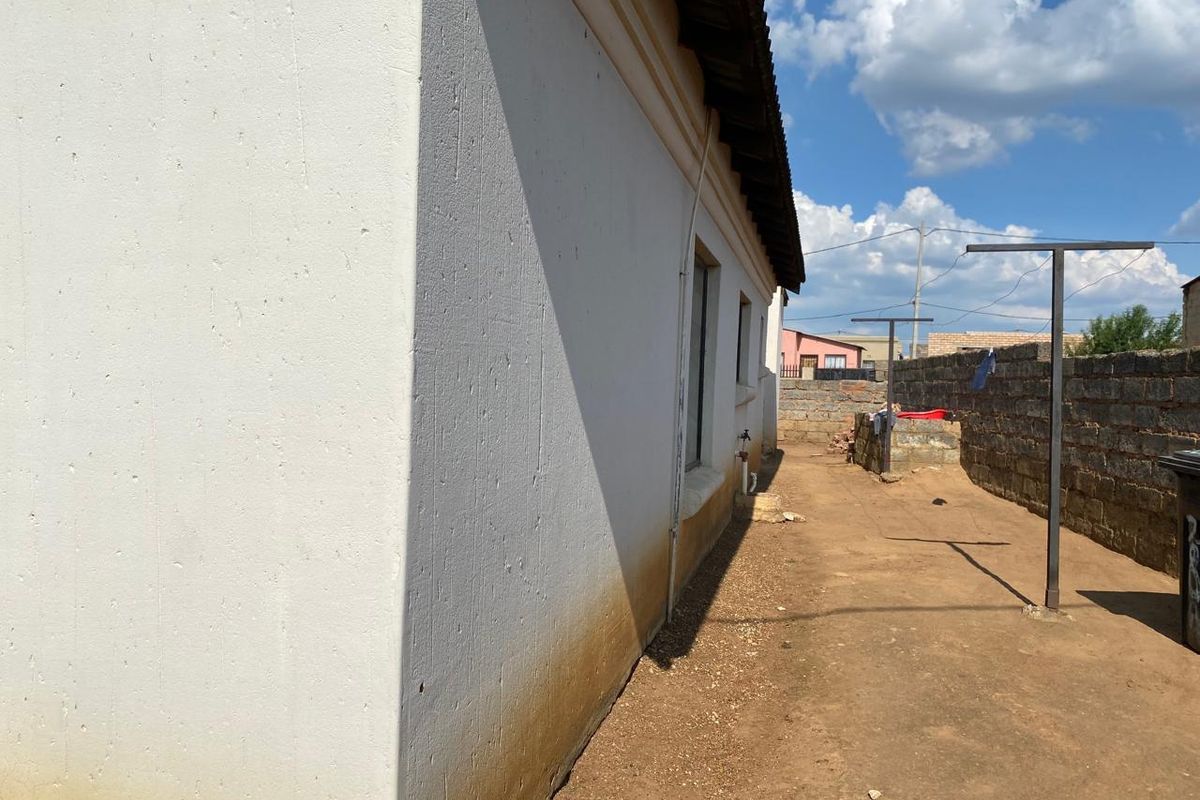 Rear exterior view of the property featuring a concrete block boundary wall, metal washing lines, and an unpaved yard area with visible wall staining.