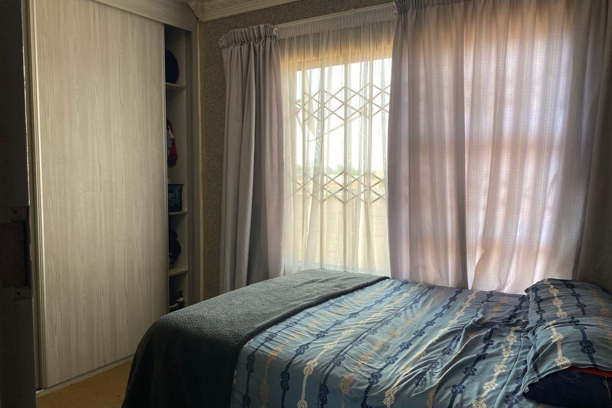 A bedroom featuring a built-in wardrobe with sliding doors, a window with a security gate, and decorative ceiling cornicing.